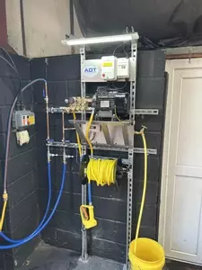 Custom wall-mounted pressure washer system with pump hardware and 20-metre hose reel installed in a vehicle detailer&rsquo;s workshop in Coalville.